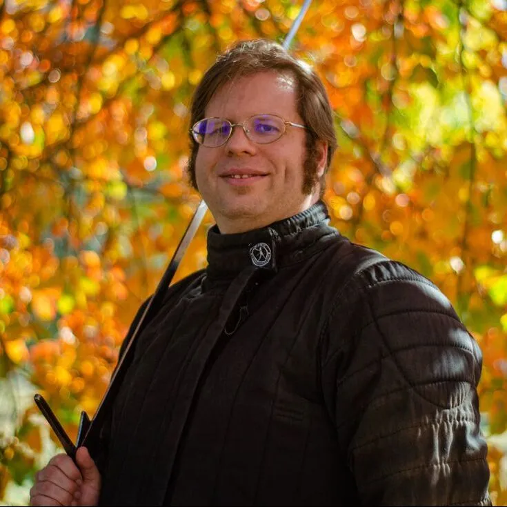John Dickens with a longsword over his shoulder among autumn leaves